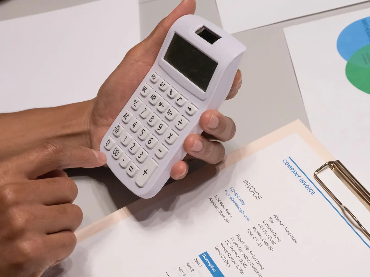 Hands using a calculator over a company invoice with line items and prices
